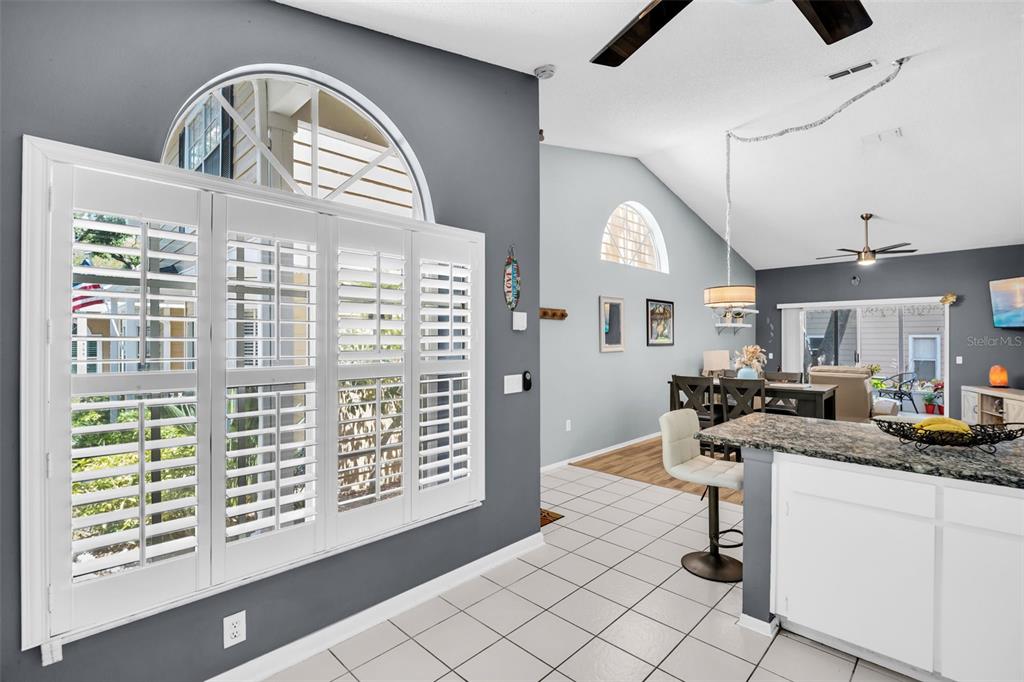 A kitchen with a breakfast bar overlooks a living area featuring vaulted ceilings and shutters — 3067 POINTER DRIVE, PALM HARBOR, FL