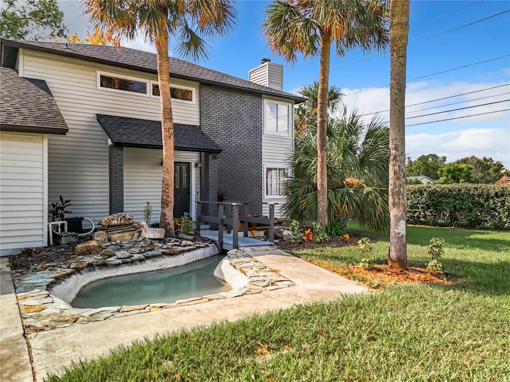 A two-story house exterior features a small pond with a stone border and wooden bridge — 1040 WAVERLY DRIVE, LONGWOOD, FL
