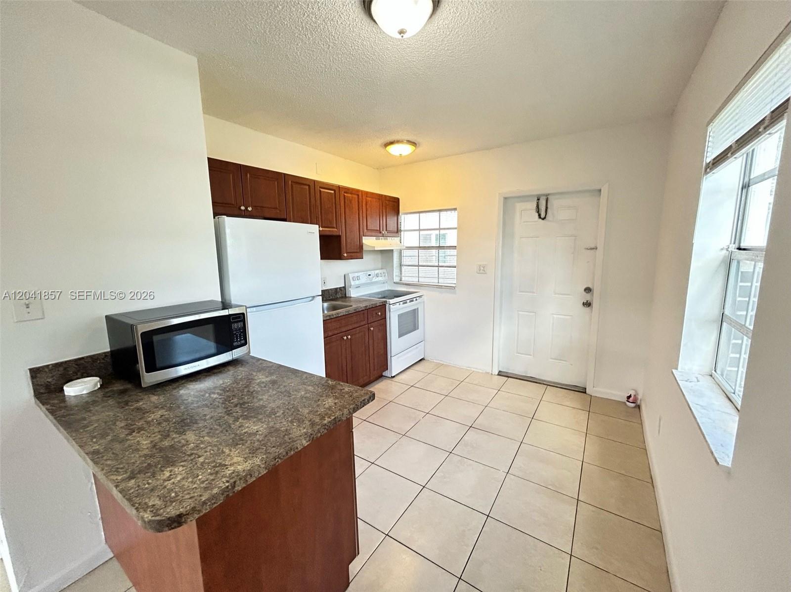A kitchen features dark wood cabinets, white appliances, a microwave, and light-colored floor tiles — 990 Phippen Waiters Rd, Dania Beach FL 33004, DANIA BEACH, FL