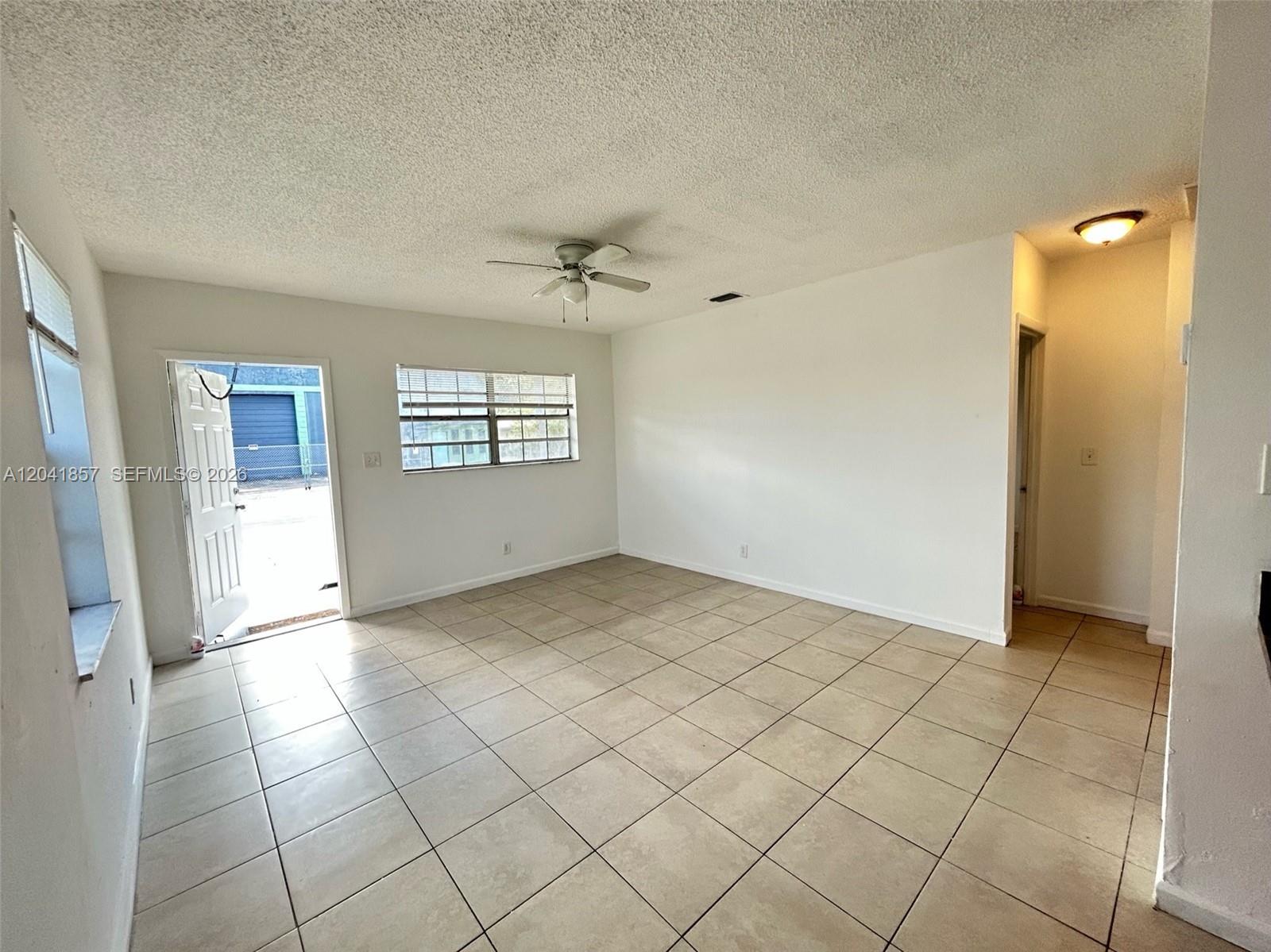 An empty room features beige tile flooring, white walls, a ceiling fan, and an open door — 990 Phippen Waiters Rd, Dania Beach FL 33004, DANIA BEACH, FL