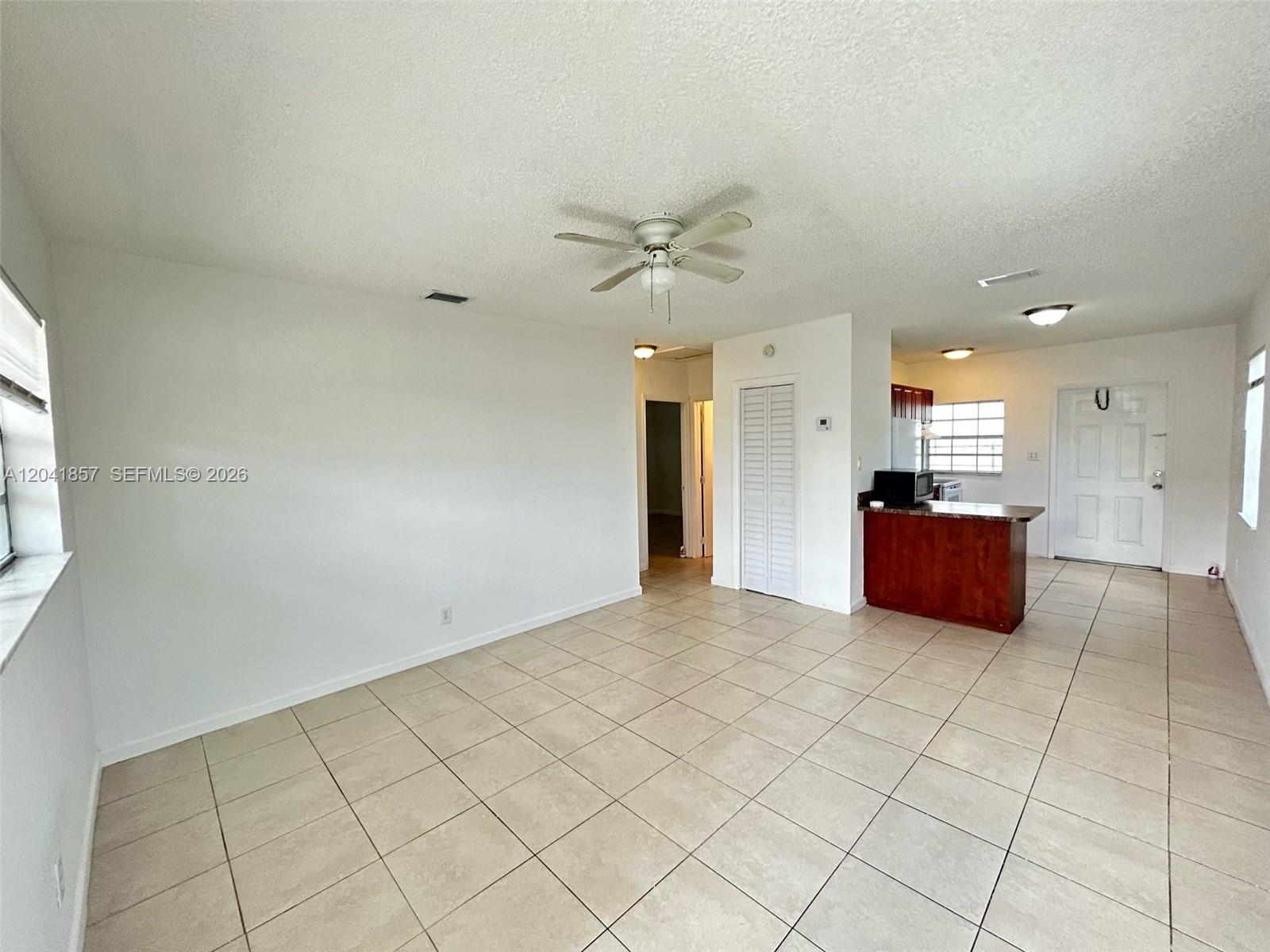 An open living area features white walls, beige tile flooring, and a ceiling fan — 990 Phippen Waiters Rd, Dania Beach FL 33004, DANIA BEACH, FL