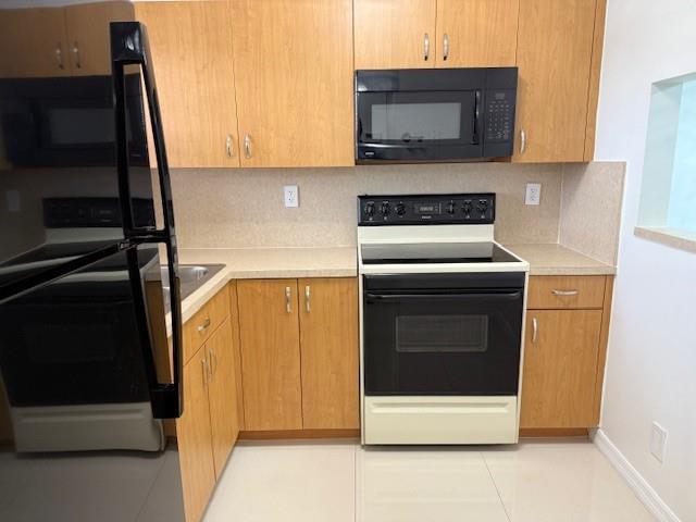 A kitchen features light wood cabinets, black appliances, and a light-colored countertop — 9660 Sunrise Lakes Boulevard # 306, Sunrise FL 33322, SUNRISE, FL