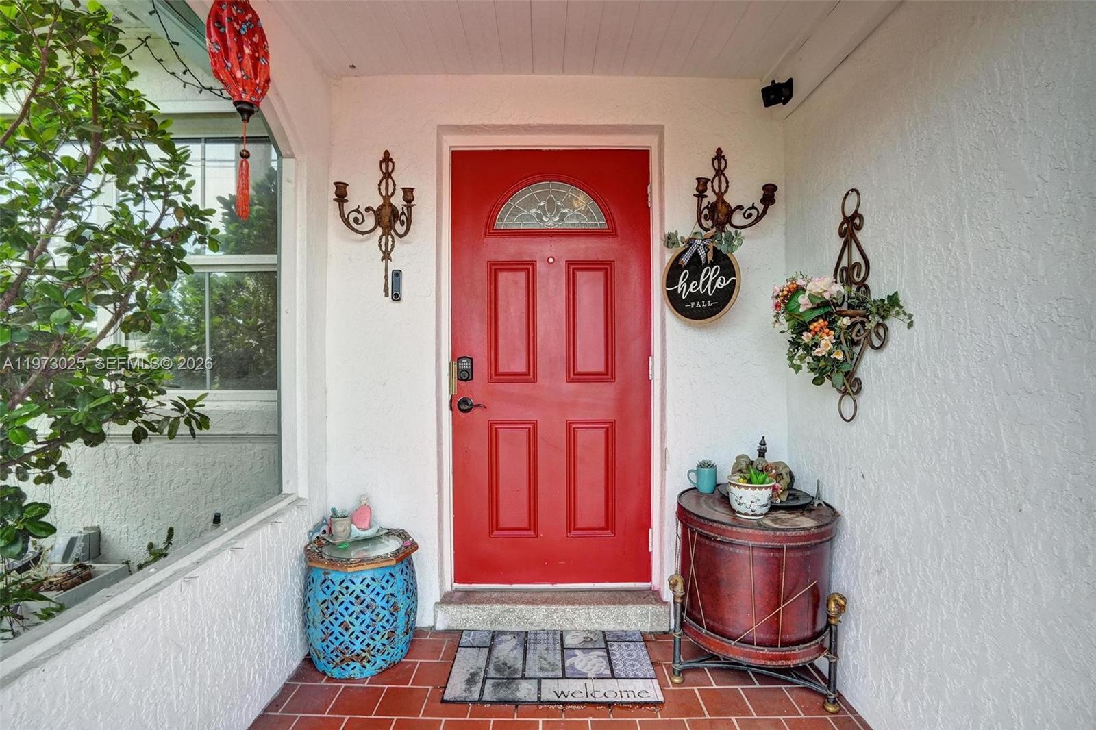 A red front door with a glass arch sits between two wall sconces on a porch — 609 SW 2nd Ave, Hallandale Beach FL 33009, HALLANDALE BEACH, FL