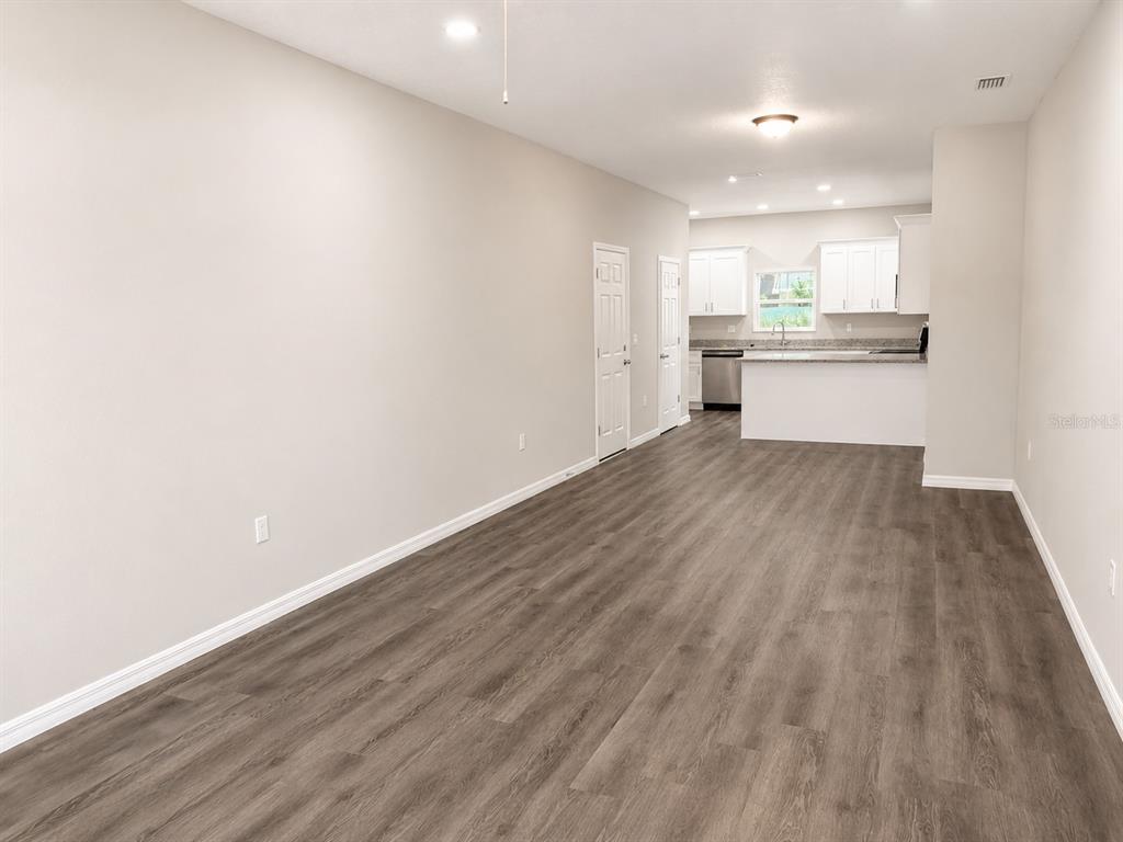 A spacious living area with wood-look flooring leads to an open kitchen with white cabinets — 5012 FINDERS CT, TAMPA, FL