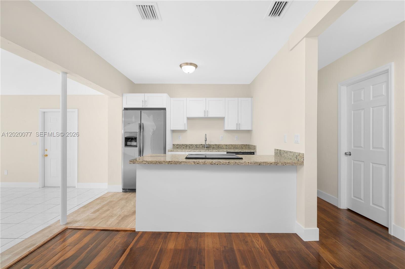 A kitchen features white cabinets, granite countertops, a stainless steel refrigerator, and wood flooring — 3271 NW 18th Ter, Miami FL 33125, MIAMI, FL