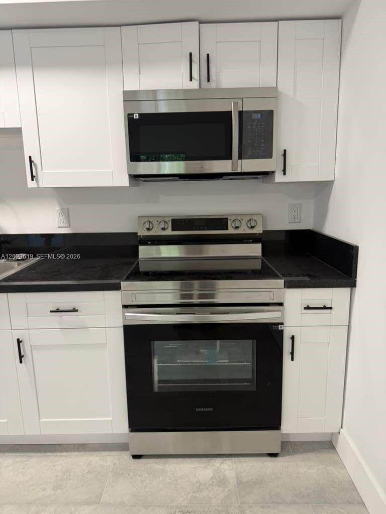 A kitchen features white cabinets, stainless steel appliances, and black countertops — 147 Nw 59th St # 304, Miami FL 33127, MIAMI, FL