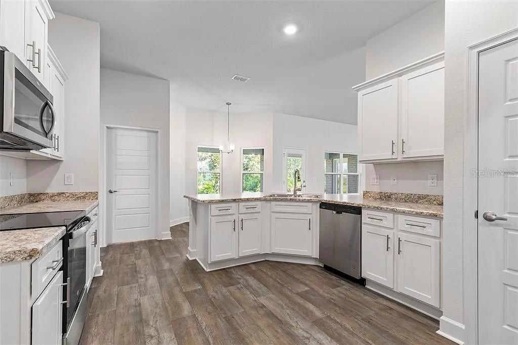 A kitchen with white cabinets, granite countertops, stainless steel appliances, and wood-look flooring — 5 PORTER LANE, PALM COAST, FL