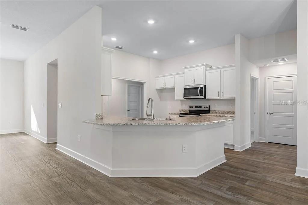 A kitchen features white cabinets, granite countertops, a breakfast bar, and wood-look flooring — 5 PORTER LANE, PALM COAST, FL