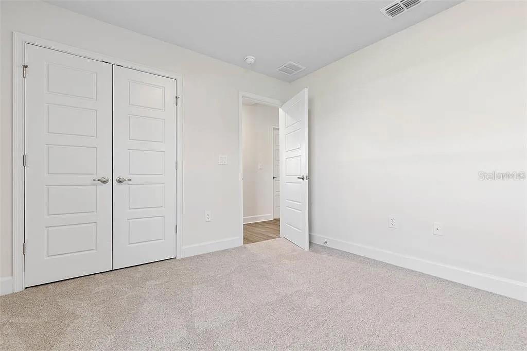 A bedroom with white walls, gray carpet, and two sets of white paneled doors — 5 PORTER LANE, PALM COAST, FL