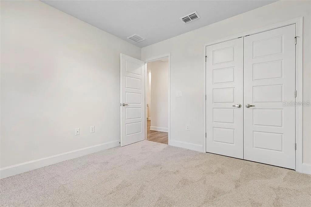 A carpeted bedroom features a white door, a double-door closet, and neutral walls — 5 PORTER LANE, PALM COAST, FL