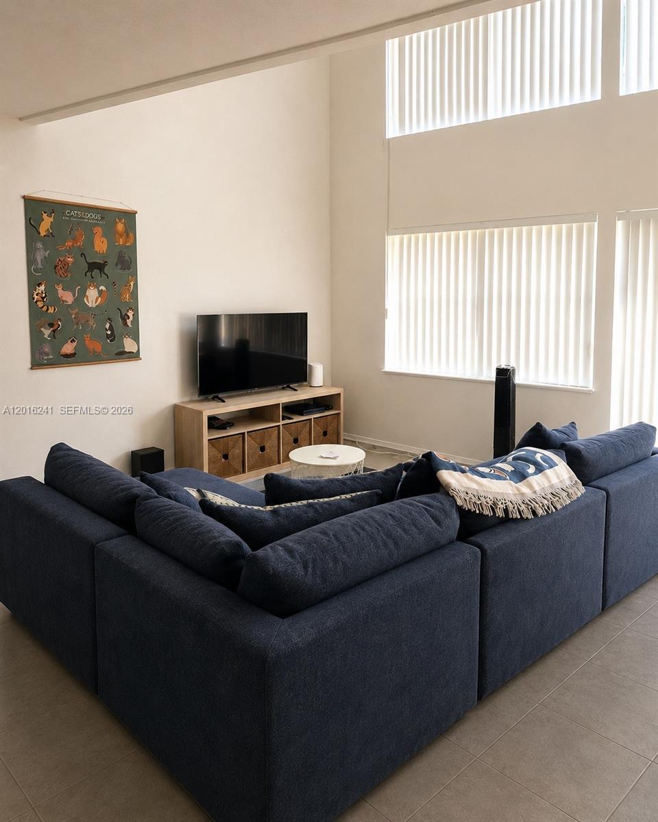 A living room features a large blue sectional sofa, a television on a wooden stand, and vertical blinds — 18051 NW 68th Ave # K201, Hialeah FL 33015, HIALEAH, FL