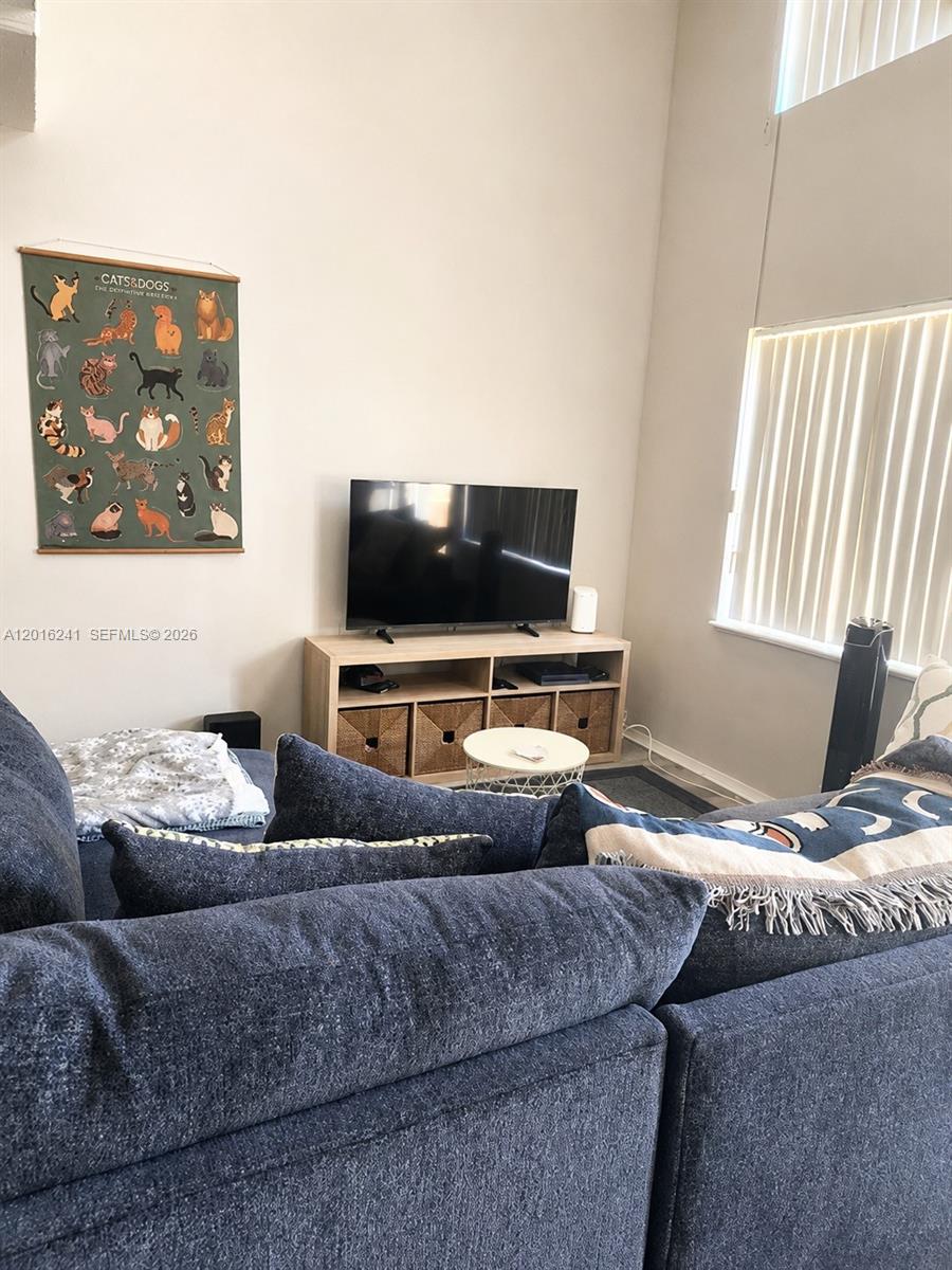 A living room features a blue sectional sofa, a television on a wooden stand, and wall art — 18051 NW 68th Ave # K201, Hialeah FL 33015, HIALEAH, FL
