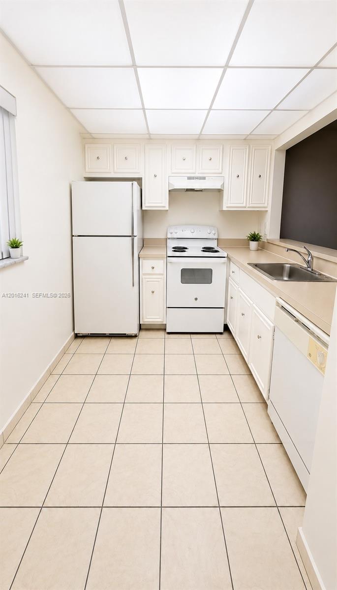 A galley kitchen features white cabinets, white appliances, beige countertops, and light-colored tile flooring — 18051 NW 68th Ave # K201, Hialeah FL 33015, HIALEAH, FL