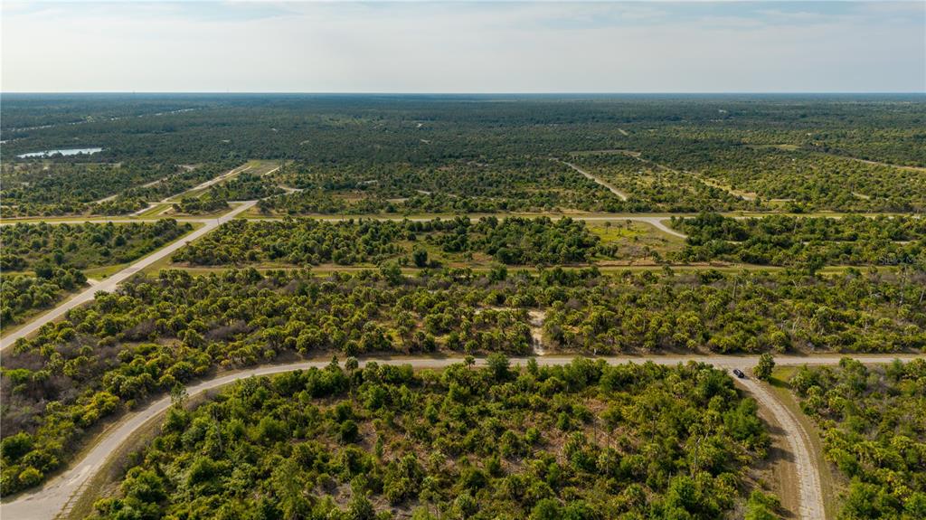 An aerial view shows a rural landscape with paved roads intersecting through dense, scrubby vegetation — 8607 FIREGLOW CIRCLE, NORTH PORT, FL