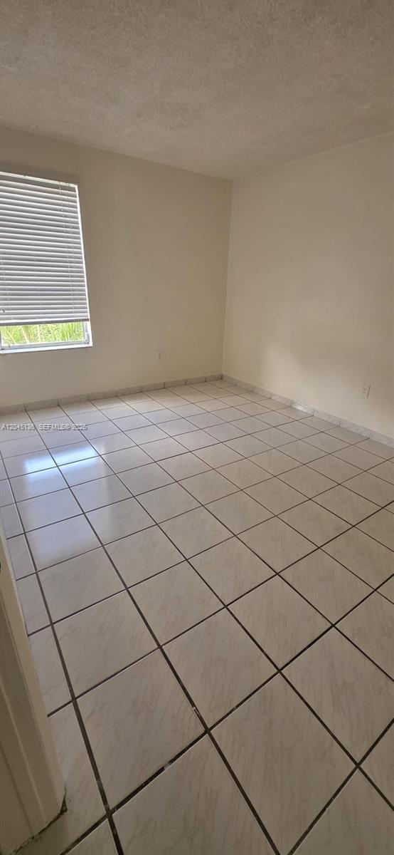 An empty room features white walls, a single window with blinds, and light-colored tiled flooring — CORAL GABLES, FL