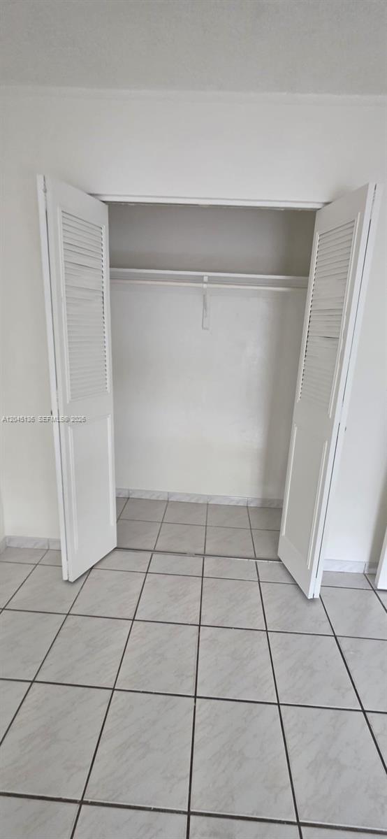 A closet with white louvered doors and a hanging rod sits above a tiled floor — CORAL GABLES, FL