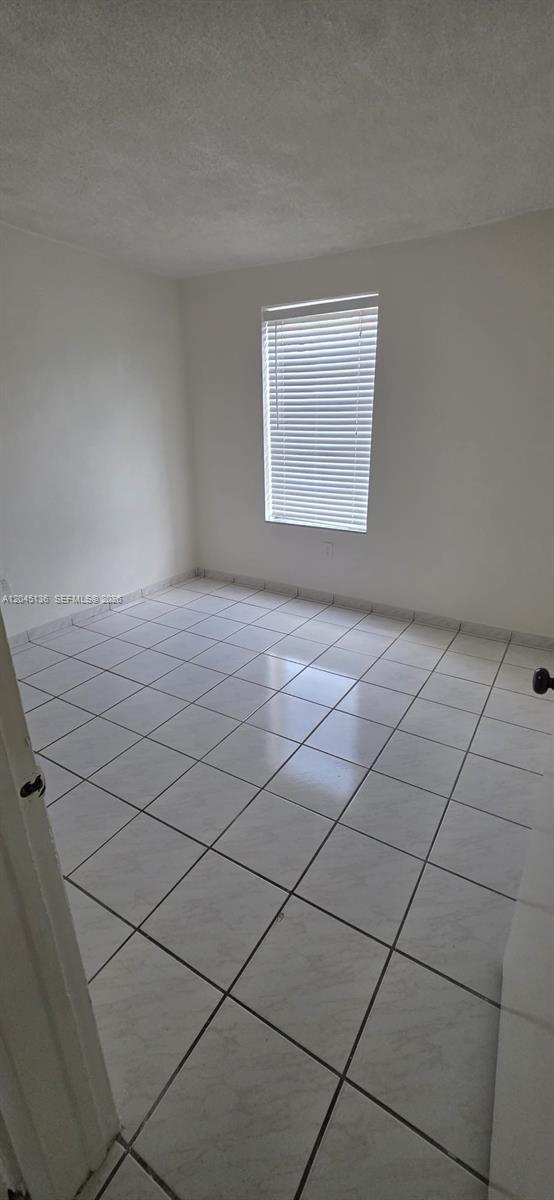 An empty room features white walls, a single window with blinds, and light-colored tiled flooring — CORAL GABLES, FL