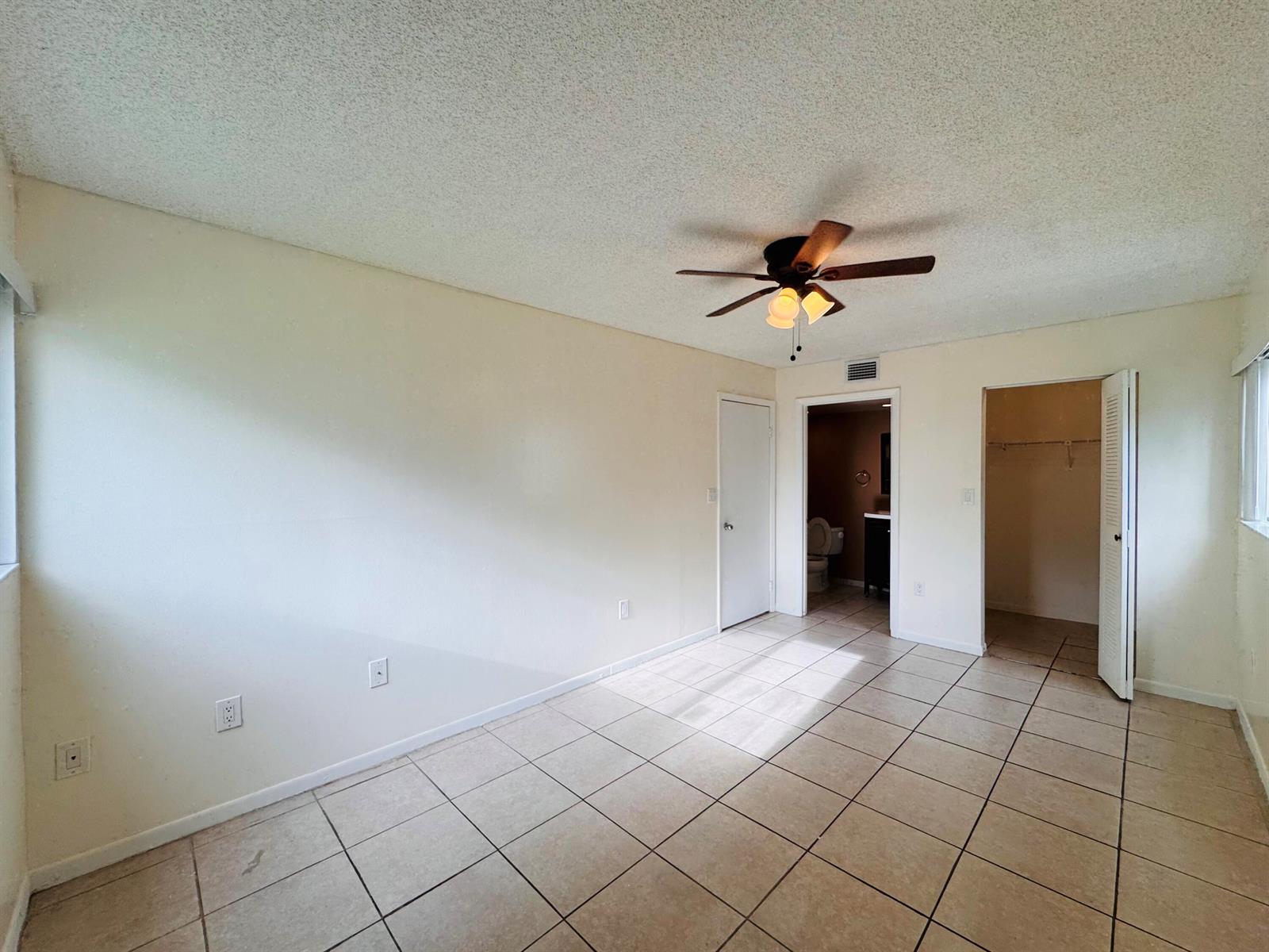 An empty bedroom features beige tile flooring, a ceiling fan, and two doorways — 20681 NE 4th Place # 105, Miami FL 33179, MIAMI, FL