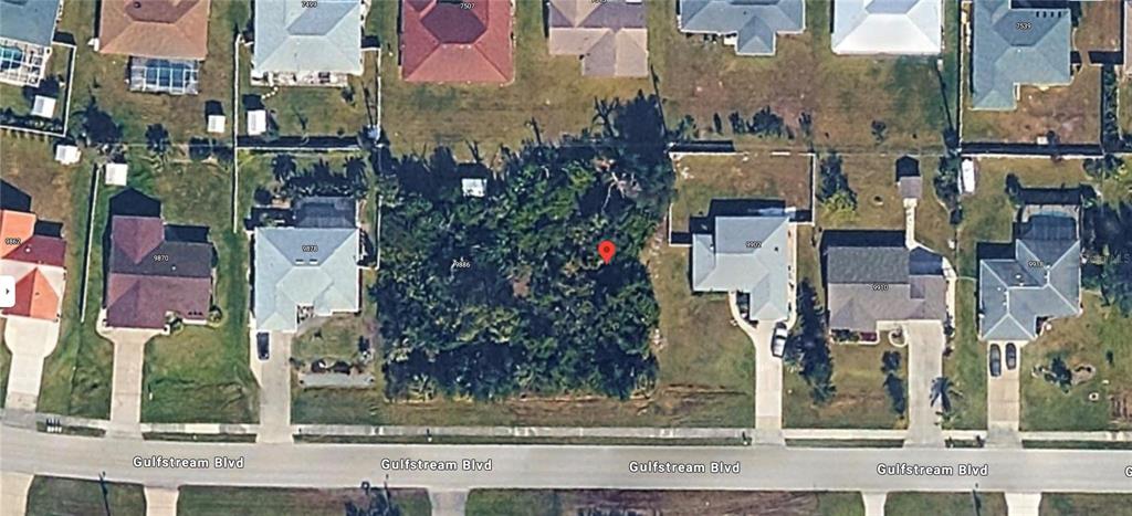 An aerial view shows a vacant, wooded residential lot situated between two houses on a street — 9894 GULFSTREAM BOULEVARD, ENGLEWOOD, FL