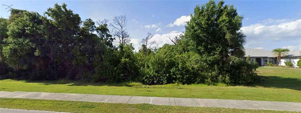 A vacant, heavily wooded residential lot sits next to a house with a grassy lawn — 9894 GULFSTREAM BOULEVARD, ENGLEWOOD, FL