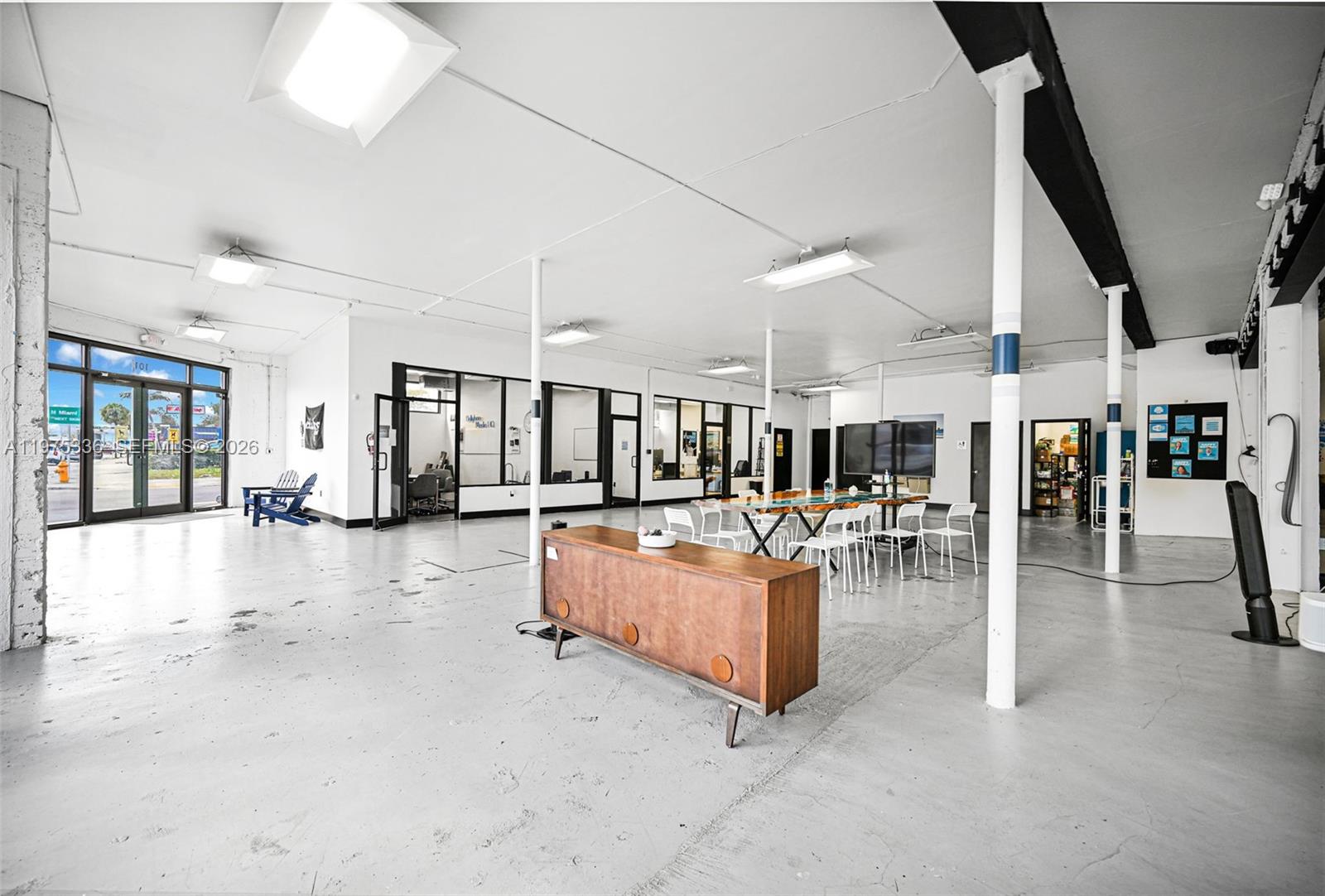 An open-plan office space features concrete floors, white walls, support columns, and glass-enclosed rooms — 101 NE 79th St, Miami FL 33138, MIAMI, FL