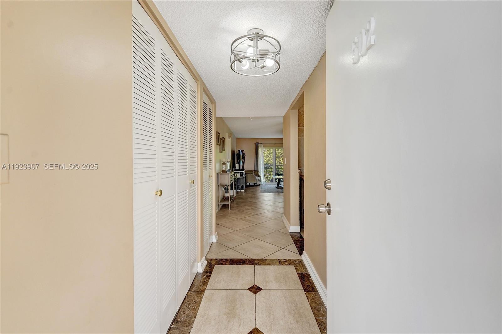 A hallway with tiled floors and louvered closet doors leads toward a living area — 4111 Stirling Rd # 502, Dania Beach FL 33314, DANIA BEACH, FL