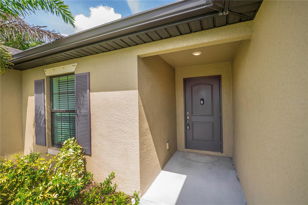 A tan stucco house exterior features a gray front door and a shuttered window — 2555 ATWATER DRIVE, NORTH PORT, FL