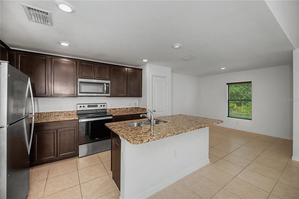 A kitchen features dark wood cabinets, granite countertops, stainless steel appliances, and a center island — 2555 ATWATER DRIVE, NORTH PORT, FL