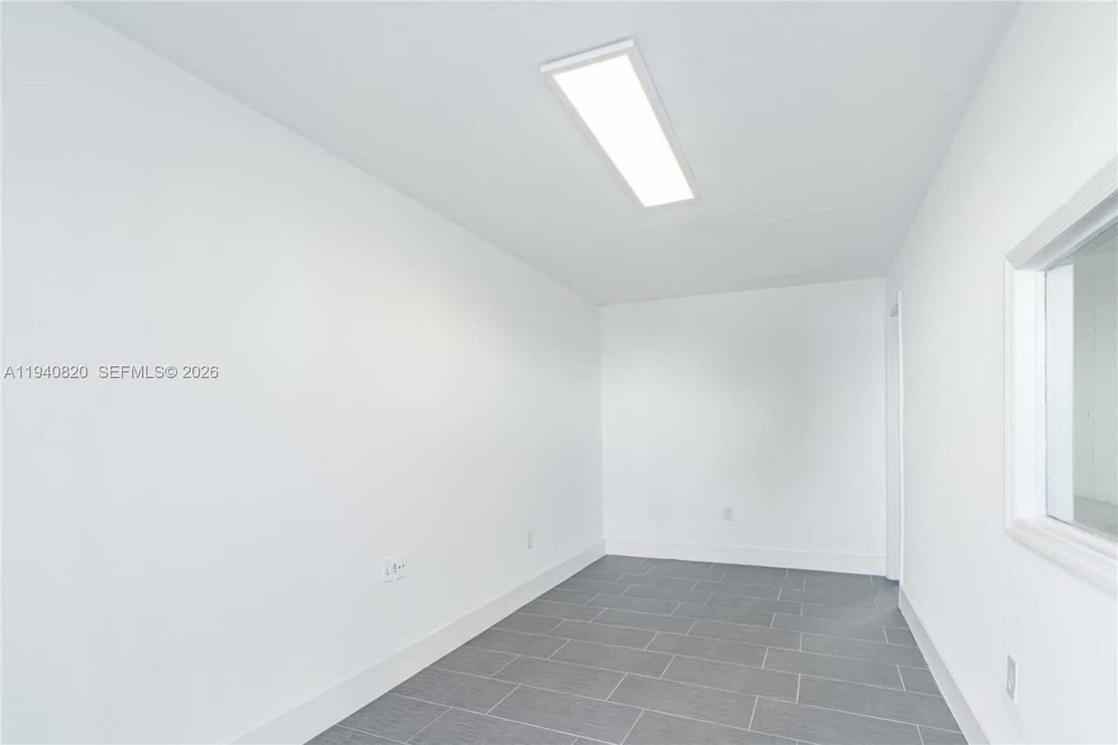 A small, empty room features white walls, a rectangular ceiling light, and gray tiled flooring — 1672 W 31st Pl, Hialeah FL 33012, HIALEAH, FL