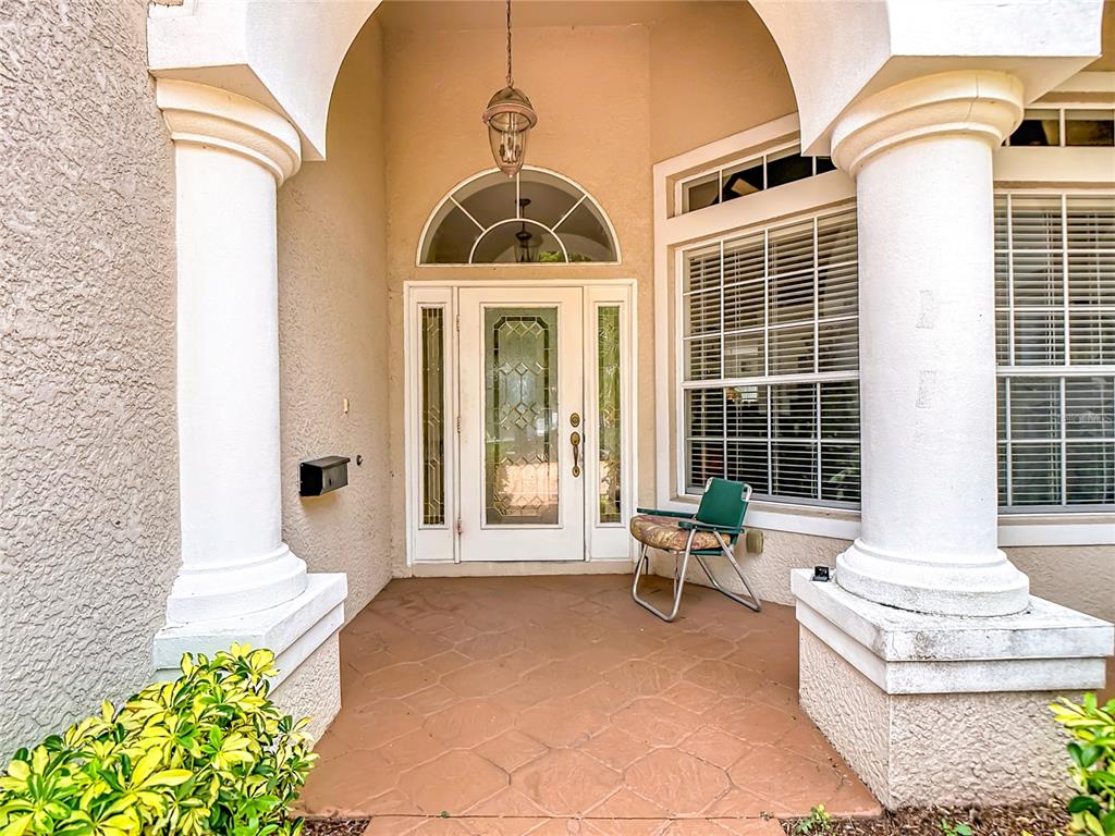 A covered entryway features a white front door with sidelights, two large columns, and a chair — 2221 OXFORD RIDGE CIRCLE, LEHIGH ACRES, FL
