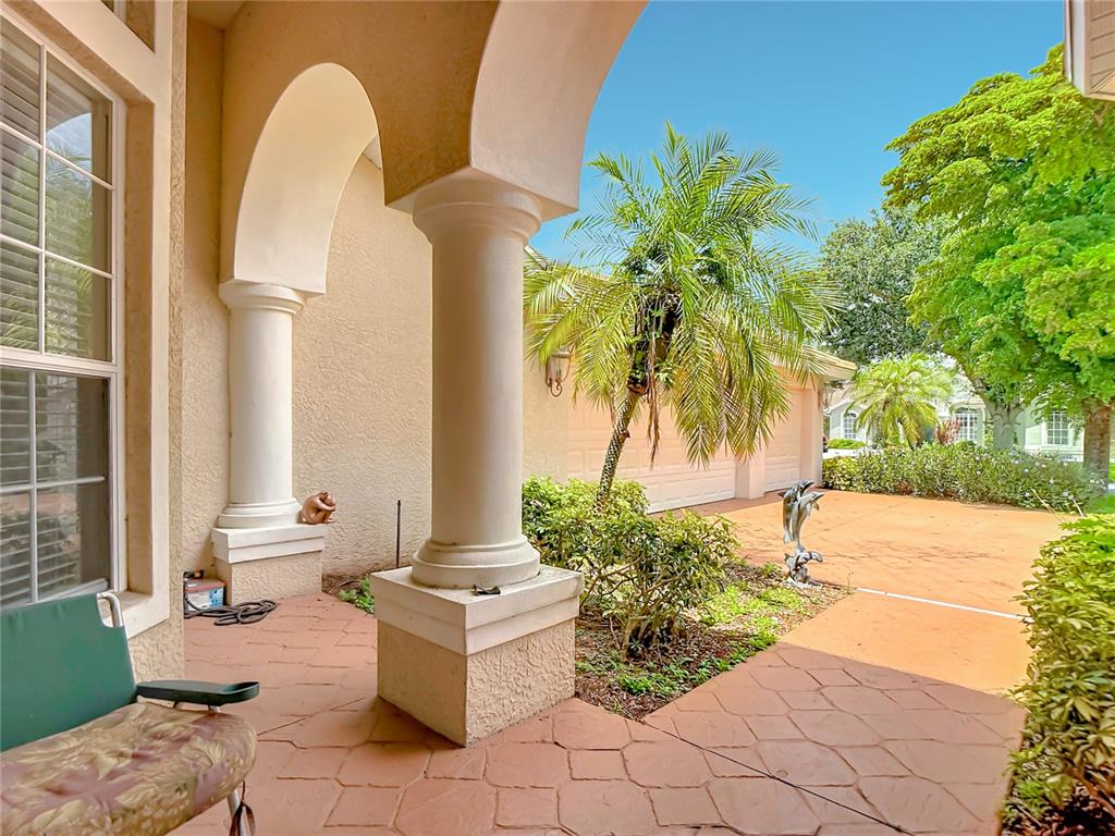 A covered patio with stone pavers, arched columns, and a view of a driveway and palm — 2221 OXFORD RIDGE CIRCLE, LEHIGH ACRES, FL