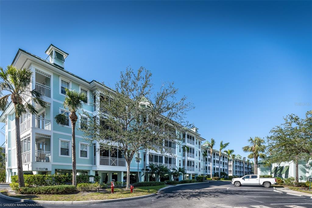 A multi-story light blue apartment building with screened balconies stands under a clear blue sky — 5125 MELBOURNE STREET UNIT E201, PUNTA GORDA, FL