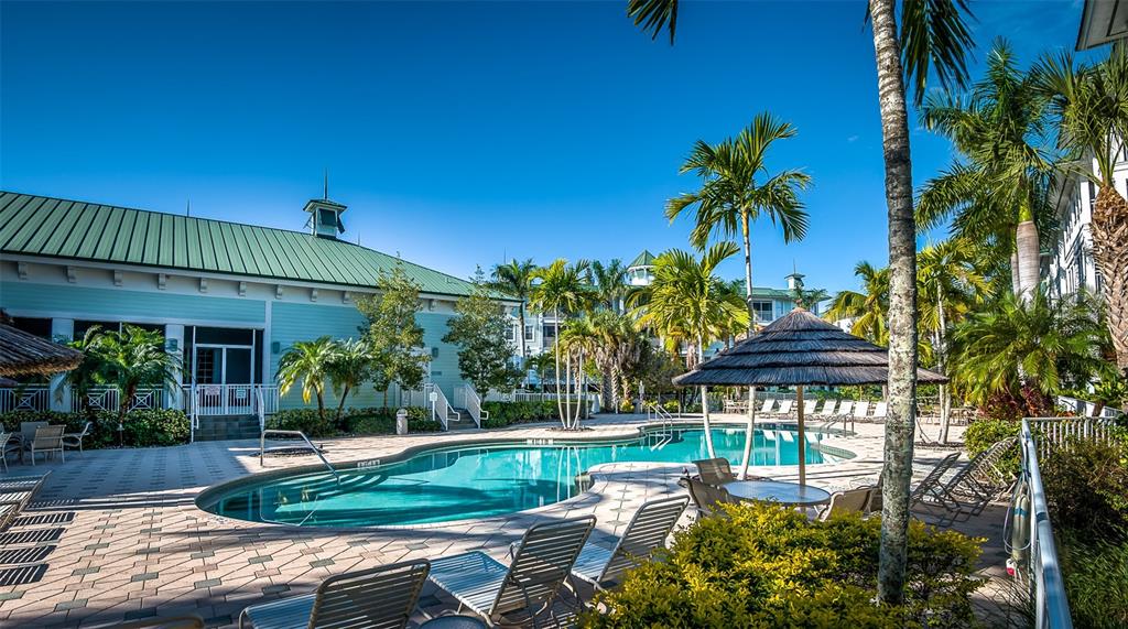 A swimming pool with a thatched umbrella sits beside a building with a green roof — 5125 MELBOURNE STREET UNIT E201, PUNTA GORDA, FL