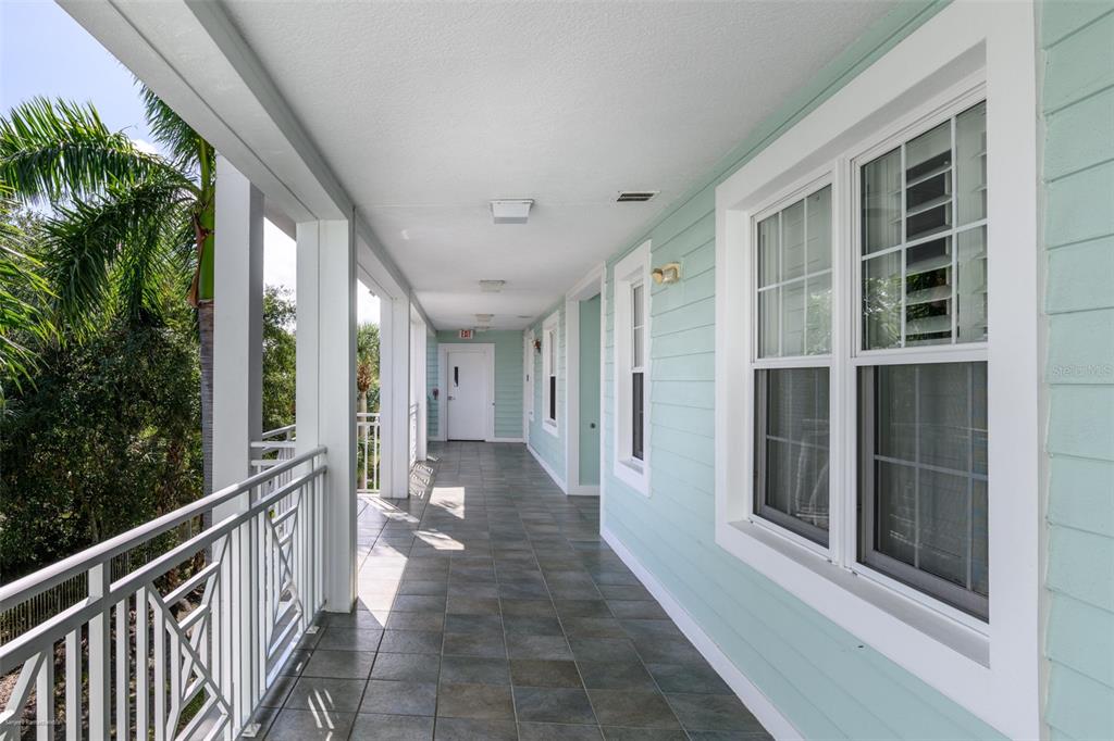 A covered outdoor balcony features light blue siding, dark tiled flooring, and a white railing — 5125 MELBOURNE STREET UNIT E201, PUNTA GORDA, FL