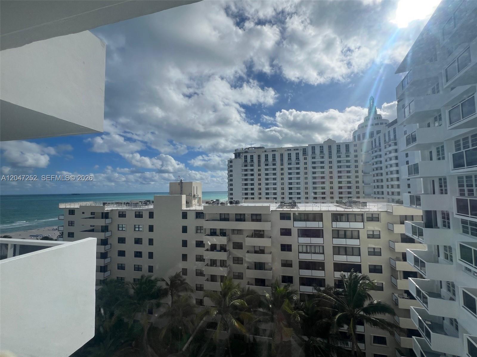 A view from a balcony overlooks a beach, palm trees, and several large apartment buildings — 100 Lincoln Rd # 1126, Miami Beach FL 33139, MIAMI BEACH, FL