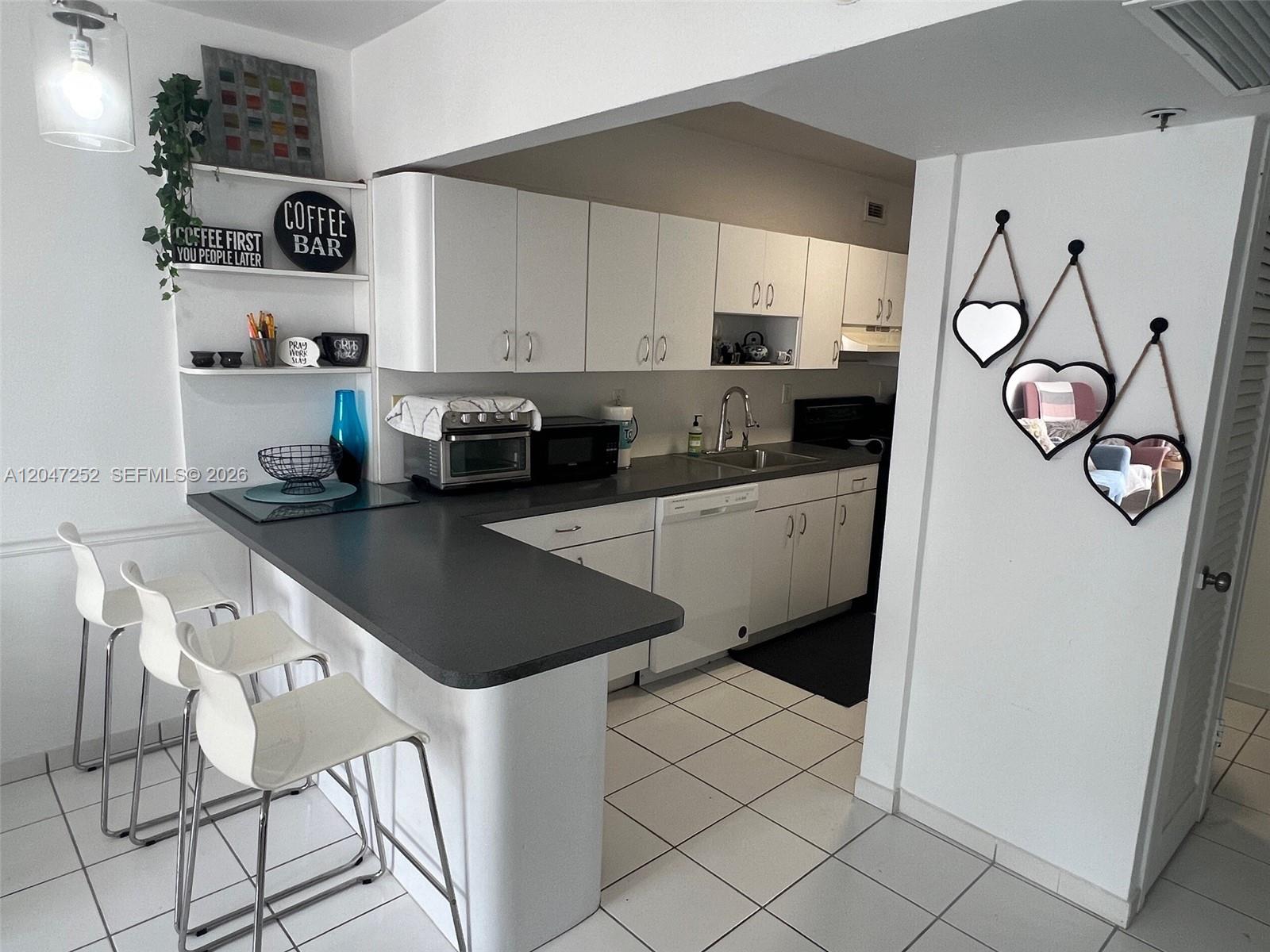 A kitchen features white cabinets, dark countertops, a breakfast bar with stools, and heart-shaped mirrors — 100 Lincoln Rd # 1126, Miami Beach FL 33139, MIAMI BEACH, FL