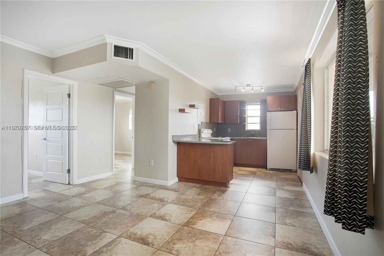A kitchen with wood cabinets and a breakfast bar opens into a tiled living area — 1020 SW 7th St # 9, Miami FL 33130, MIAMI, FL