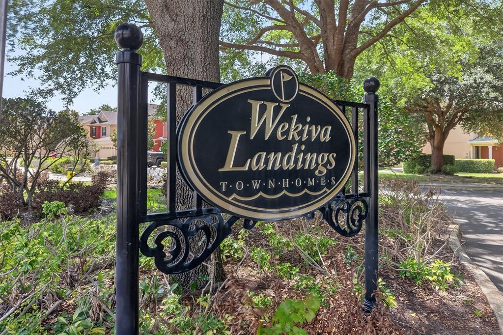 A black metal sign for Wekiva Landings Townhomes stands outdoors near trees and a road — 145 STENHOUSE LANE, LONGWOOD, FL