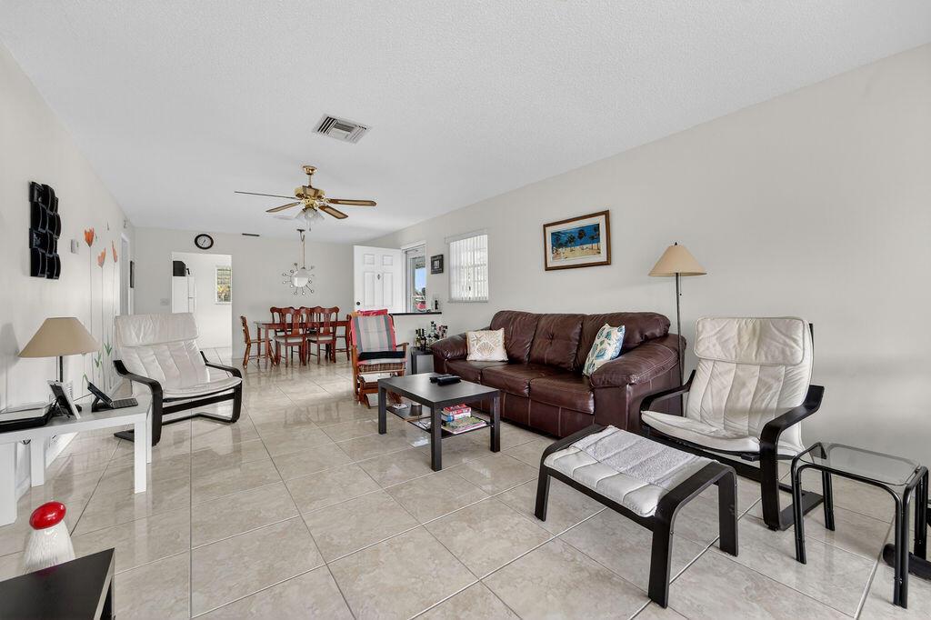 A living room with tile floors, a brown leather sofa, and two white accent chairs — 622 Hummingbird Lane, Delray Beach FL 33445, DELRAY BEACH, FL