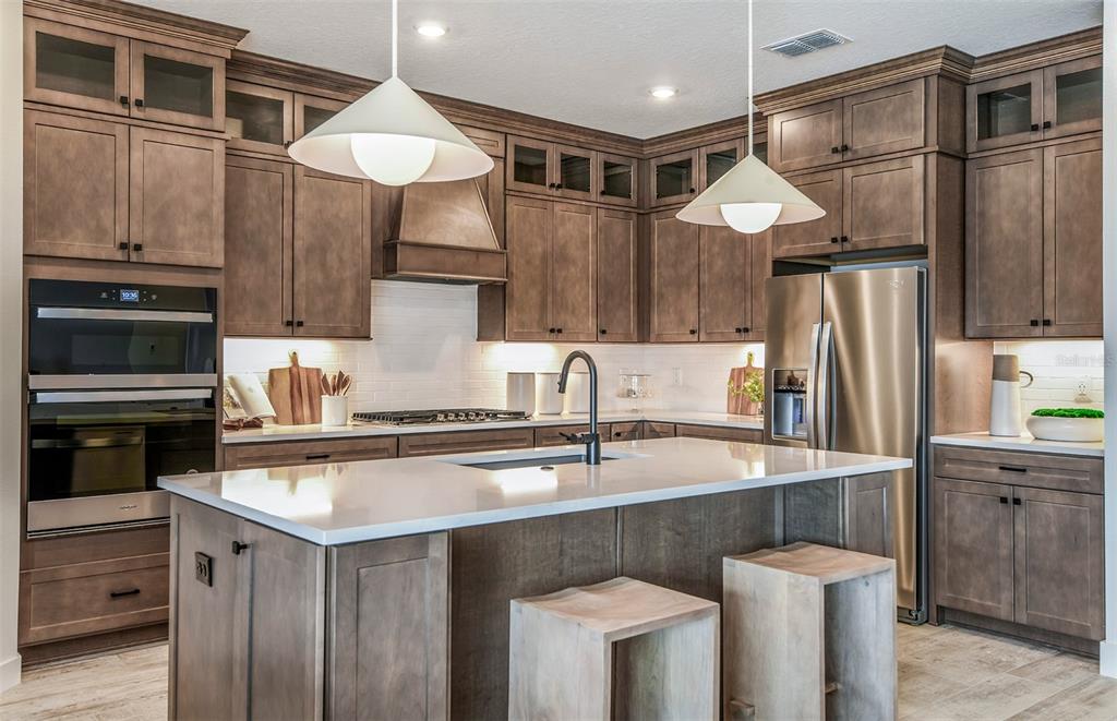 A modern kitchen features wood cabinets, a white quartz island, and stainless steel appliances — 6840 GILLY SHADOW STREET, WESLEY CHAPEL, FL