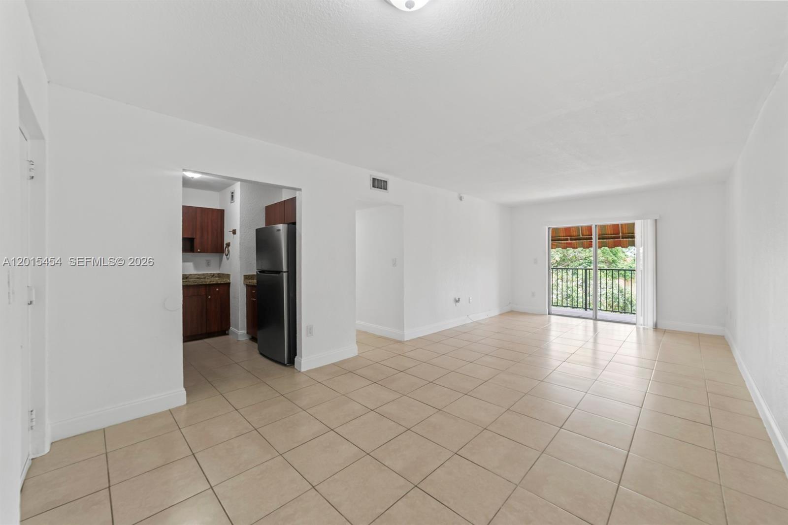 An open living area features beige tile flooring, white walls, and an adjacent kitchen — 525 W 69th St # 306, Hialeah FL 33014, HIALEAH, FL
