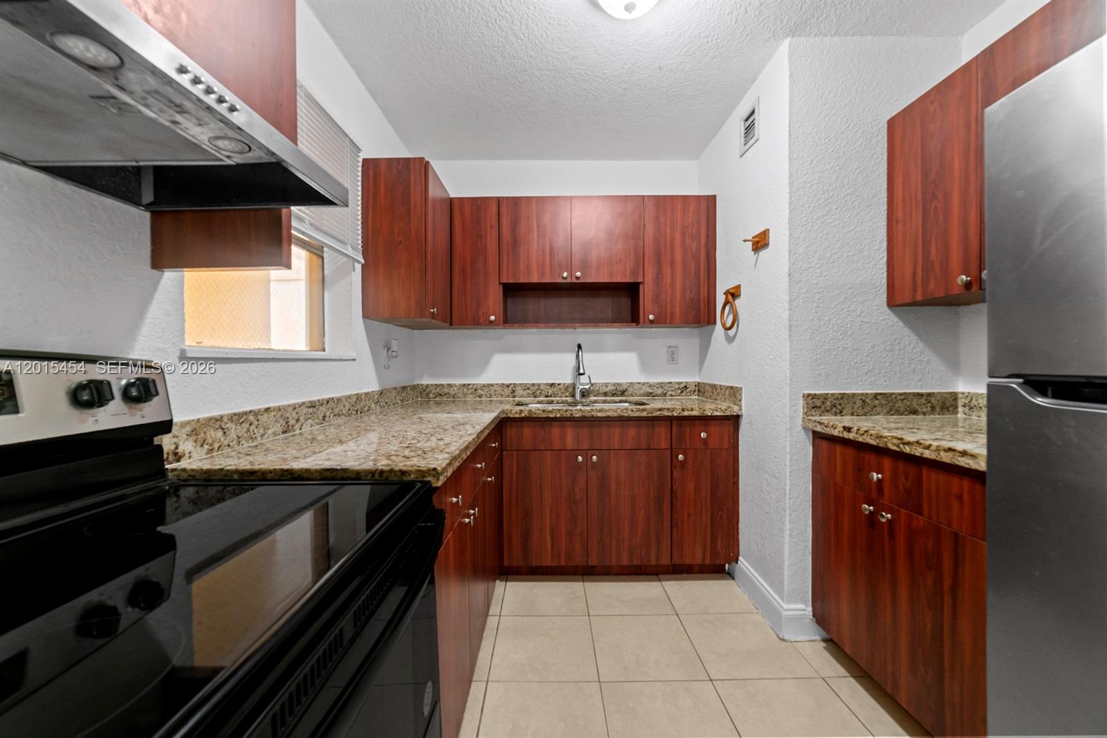 A kitchen features wood cabinets, granite countertops, a stainless steel refrigerator, and tile flooring — 525 W 69th St # 306, Hialeah FL 33014, HIALEAH, FL