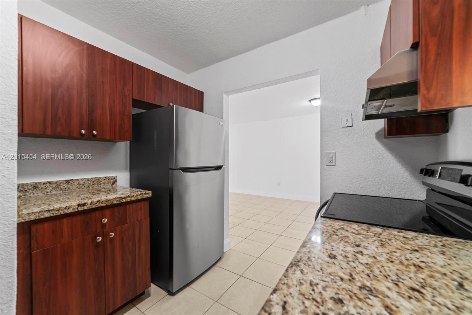 A kitchen features wood cabinets, granite countertops, stainless steel appliances, and tile flooring — 525 W 69th St # 306, Hialeah FL 33014, HIALEAH, FL