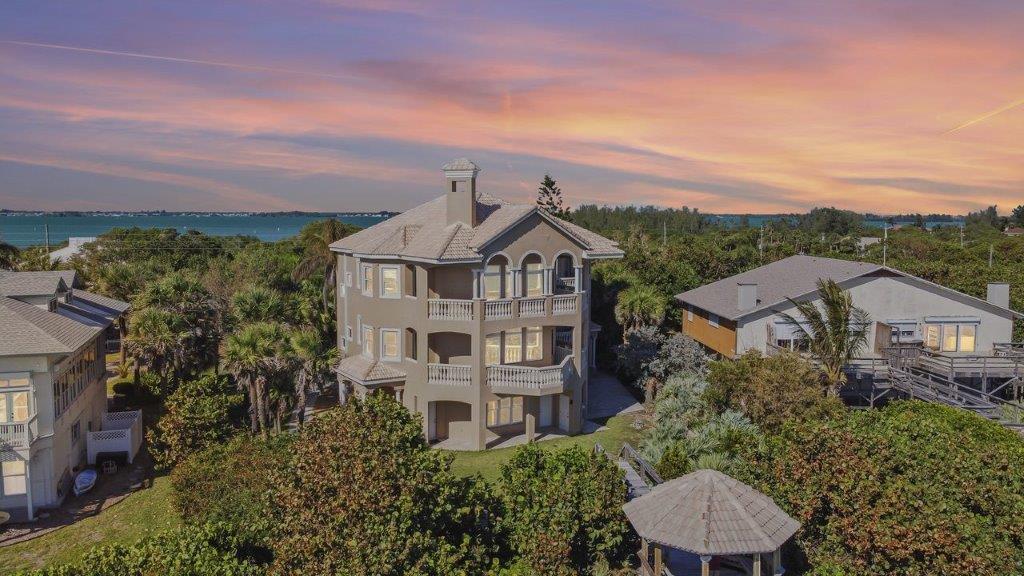 An aerial view of a multi-story coastal home surrounded by trees near the water — 8327 Jimmy Buffett Mem Highway, Melbourne Beach FL 32951, MELBOURNE BEACH, FL