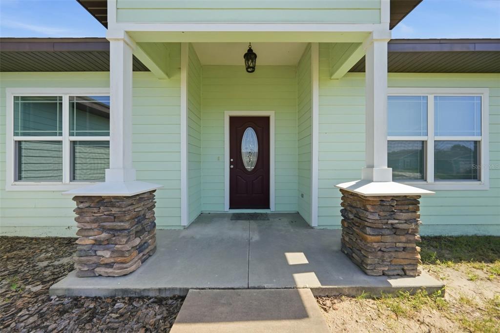 The exterior of a house features a covered porch with stone-based columns and a door — 23051 NW 4TH PLACE, NEWBERRY, FL