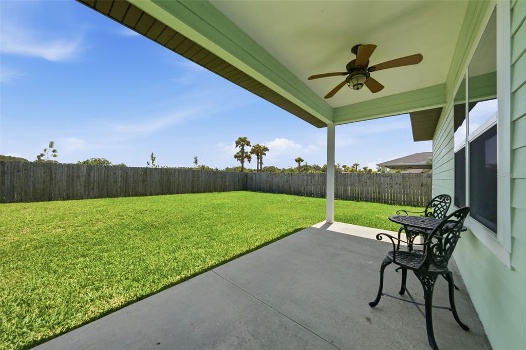 A covered concrete patio overlooks a fenced backyard with a lawn and a ceiling fan — 23051 NW 4TH PLACE, NEWBERRY, FL