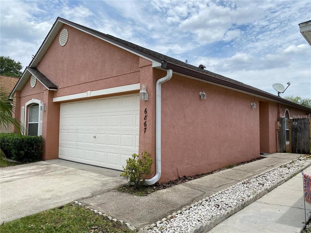 A single-story house with a pink stucco exterior, a white garage door, and a concrete driveway — 6867 BELMAR DRIVE, ORLANDO, FL