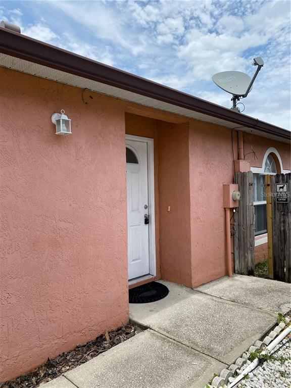 A salmon-colored exterior wall features a white front door, a light fixture, and a satellite dish — 6867 BELMAR DRIVE, ORLANDO, FL