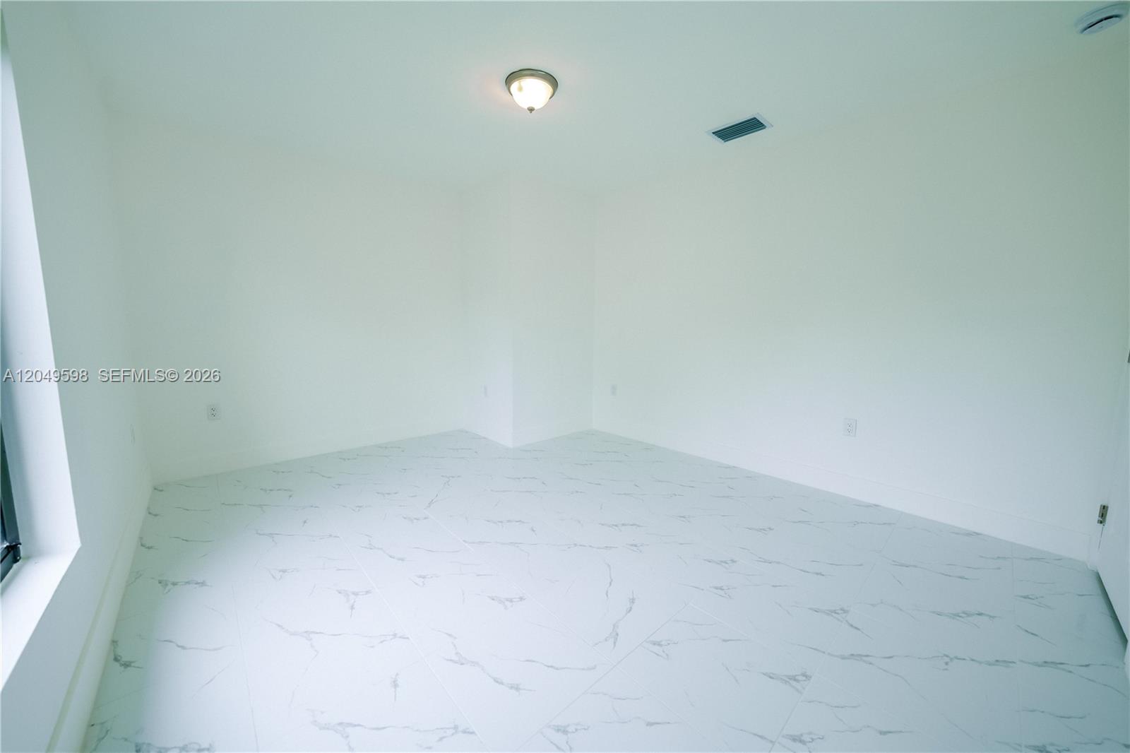 An empty room features white walls, a ceiling light, and white marble-patterned tile flooring — 1112 NW 81st St, Miami FL 33150, MIAMI, FL