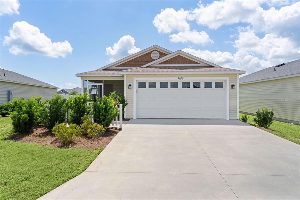 A single-story house with a two-car garage, light siding, and a screened-in front porch — 7185 FAY COURT, THE VILLAGES, FL
